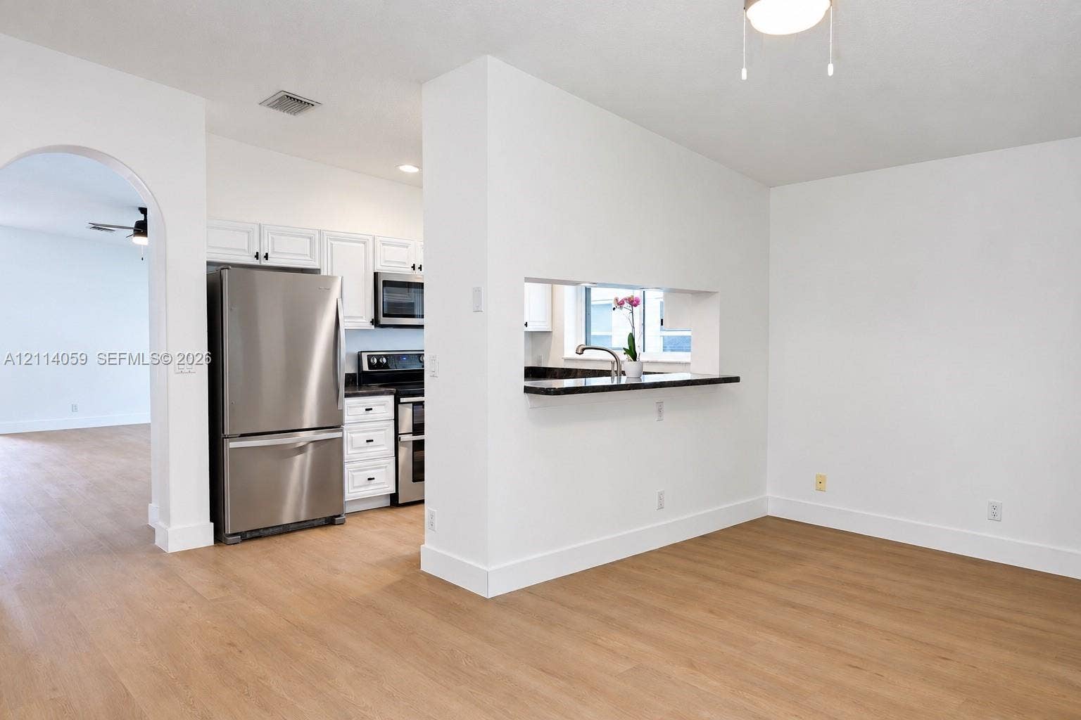8023 N Tranquility Lake Drive, Delray Beach, FL 33446 Kitchen featuring stainless steel appliances, white cabinetry, dark stone-finish countertops, and wood-finish flooring, complemented by an arched doorway