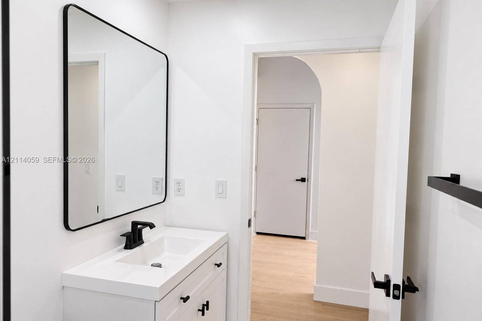 8023 N Tranquility Lake Drive, Delray Beach, FL 33446 Modern white vanity with a rectangular sink, matte black faucet, rounded rectangular mirror, and matte black hardware featuring an arched doorway entry