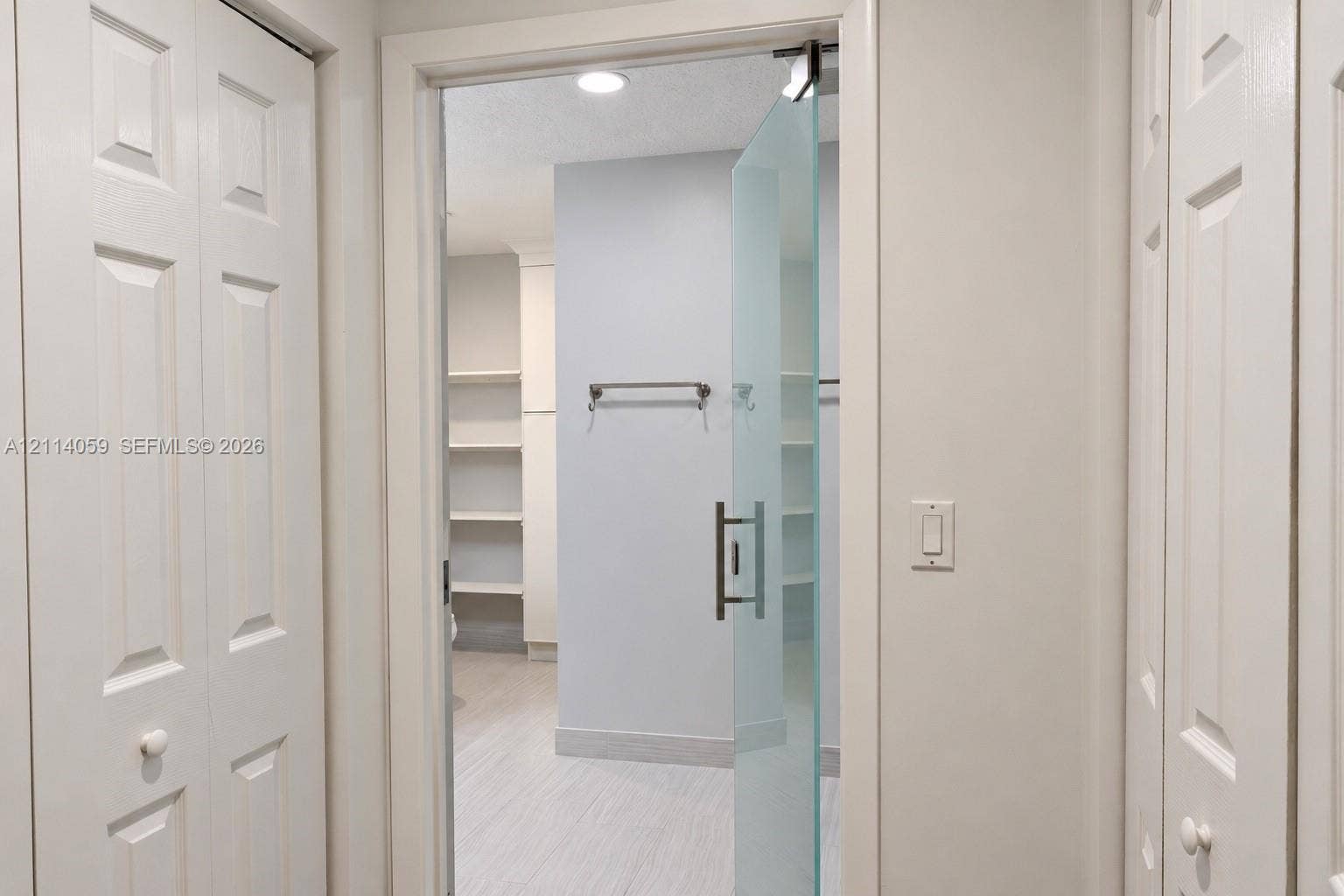 8023 N Tranquility Lake Drive, Delray Beach, FL 33446 Frameless frosted glass door with a brushed metal handle, recessed ceiling lighting, built-in open shelving, and dual white paneled folding doors