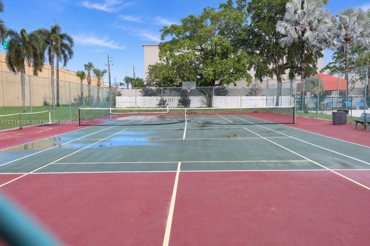 8023 N Tranquility Lake Drive, Delray Beach, FL 33446 Tennis court with perimeter chain-link fencing, dual-tone hard surfacing, and integrated basketball goal