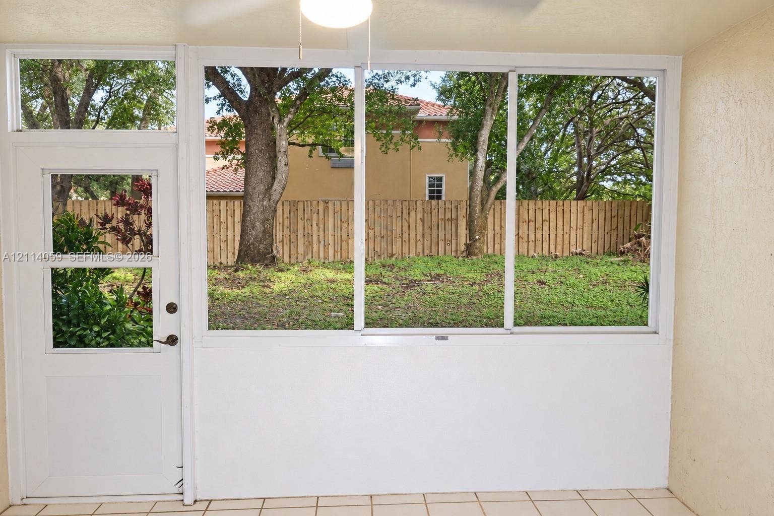 8023 N Tranquility Lake Drive, Delray Beach, FL 33446 Enclosed sunroom featuring large pane windows, tile flooring, a ceiling-mounted light fixture, and an exterior door providing access to the fenced backyard