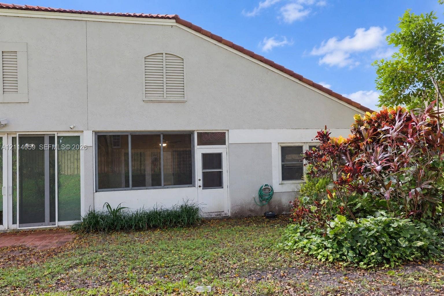 8023 N Tranquility Lake Drive, Delray Beach, FL 33446 Stucco exterior featuring arched louvered shutters, red tile roof accents, multi-pane sliding glass doors, and a screened enclosure
