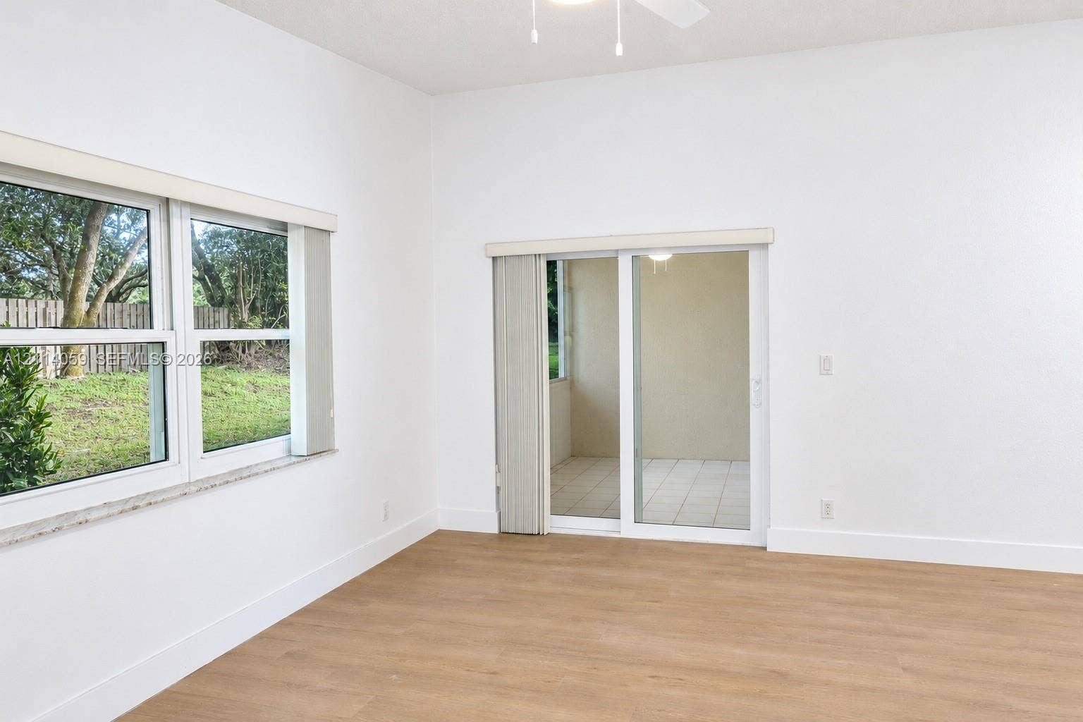 8023 N Tranquility Lake Drive, Delray Beach, FL 33446 Interior space featuring wood-finish flooring, vaulted ceilings, dual-pane windows, and sliding glass doors opening to a tiled patio