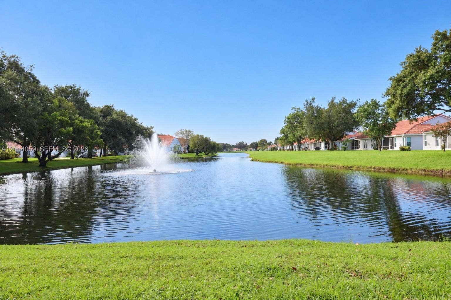 8023 N Tranquility Lake Drive, Delray Beach, FL 33446 Waterfront setting featuring a central fountain, manicured lawn, and mature canopy trees