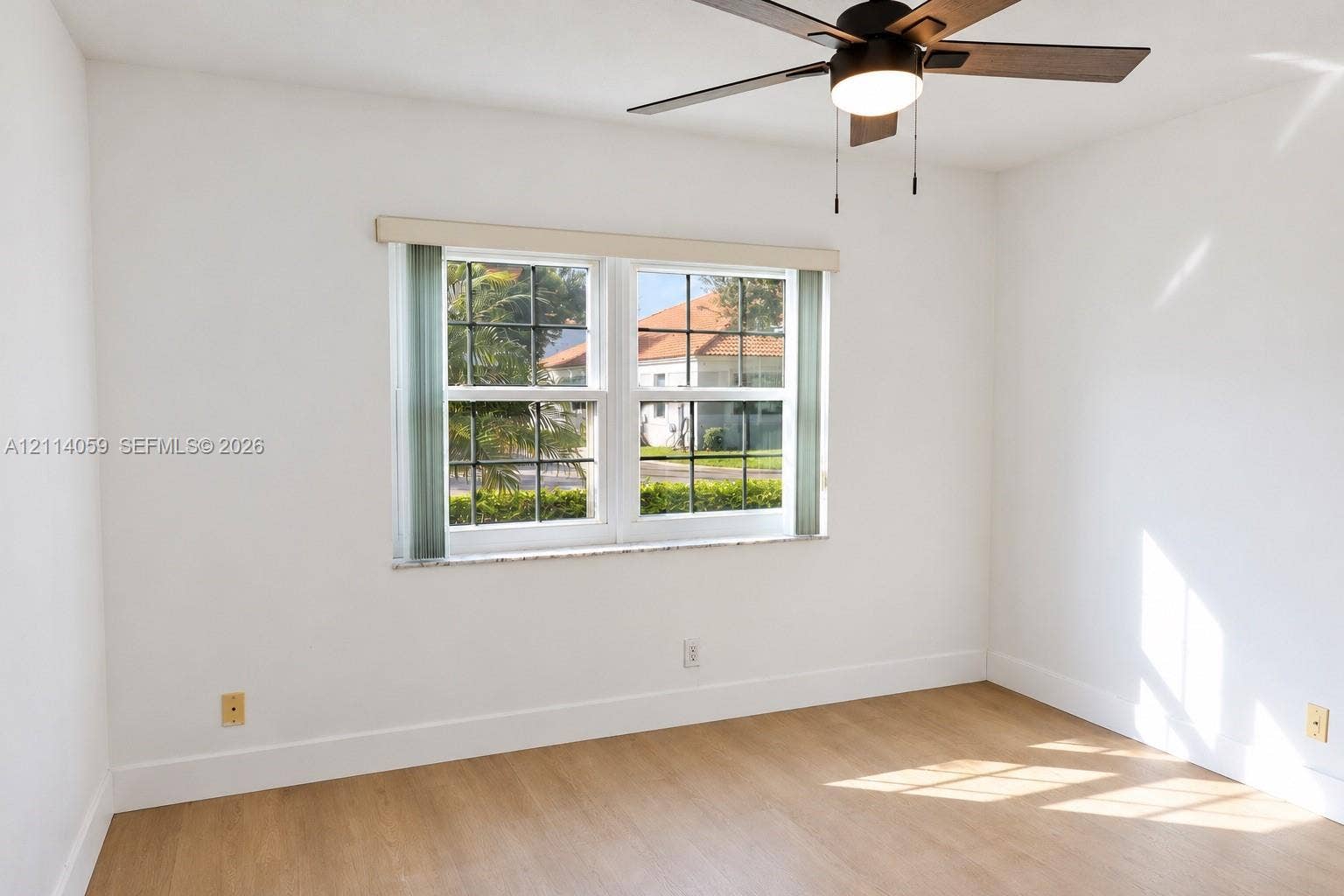 8023 N Tranquility Lake Drive, Delray Beach, FL 33446 Room interior featuring wood-finish flooring, white walls, dual-pane windows with muntins, and a ceiling fan with integrated lighting