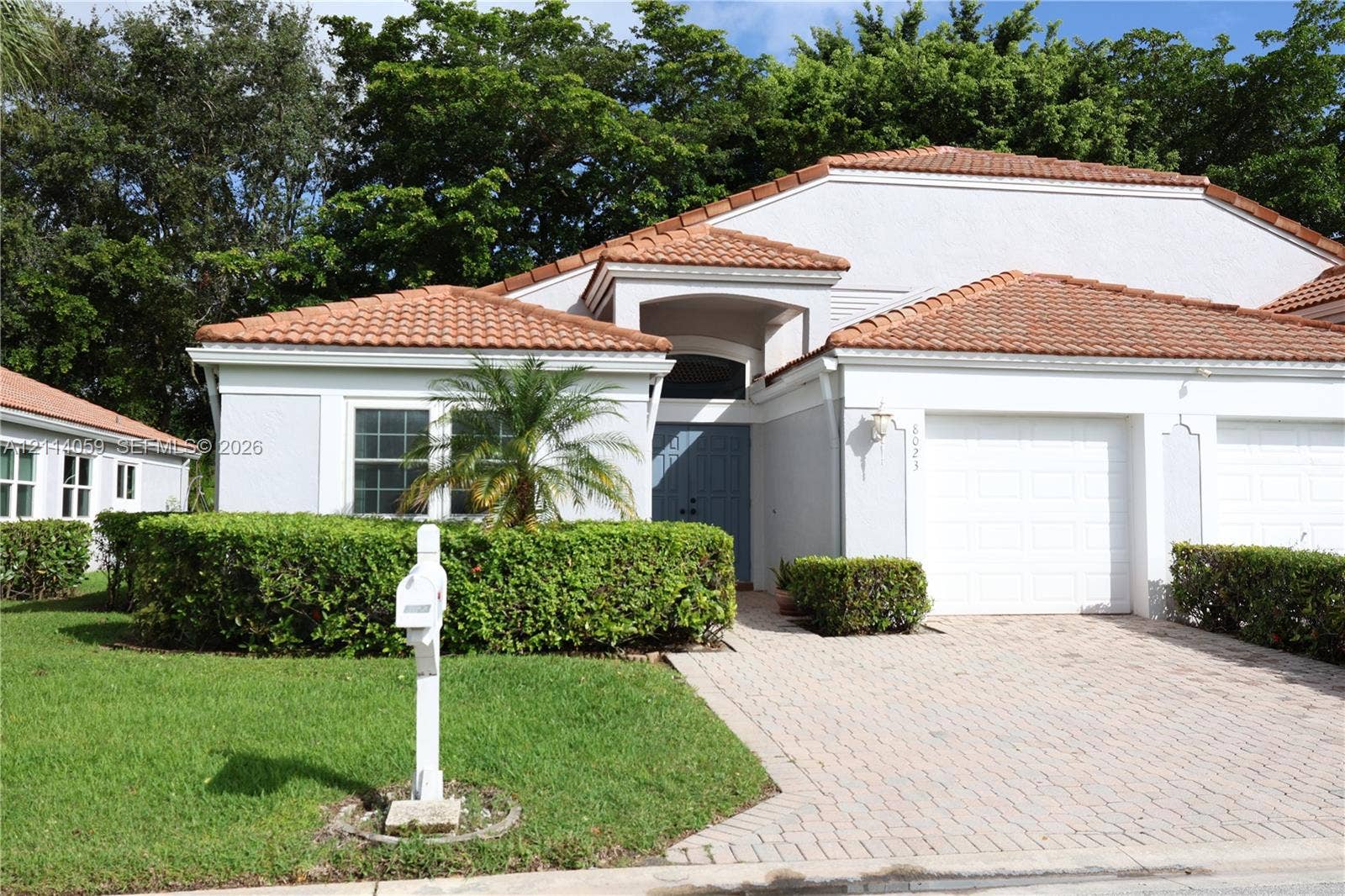 8023 N Tranquility Lake Drive, Delray Beach, FL 33446 Single-story exterior featuring a terracotta tile roof, paver driveway, recessed entry, and manicured shrubbery