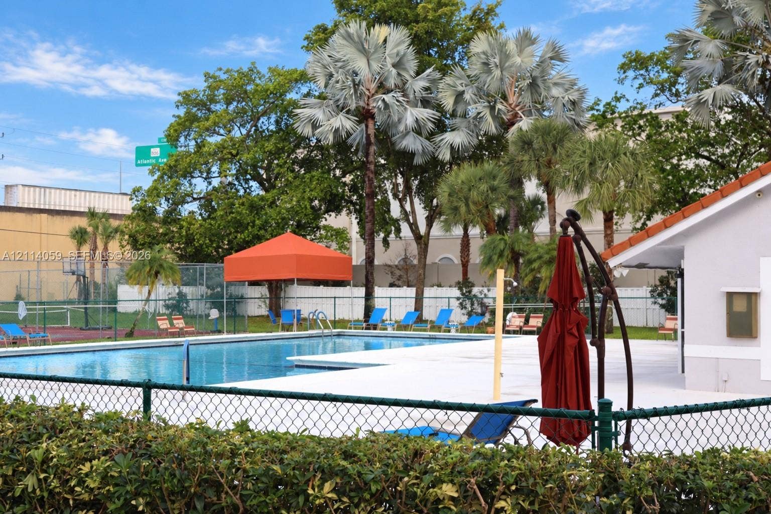 8023 N Tranquility Lake Drive, Delray Beach, FL 33446 Swimming pool with concrete deck, chain-link perimeter fencing, and tennis court with backboard