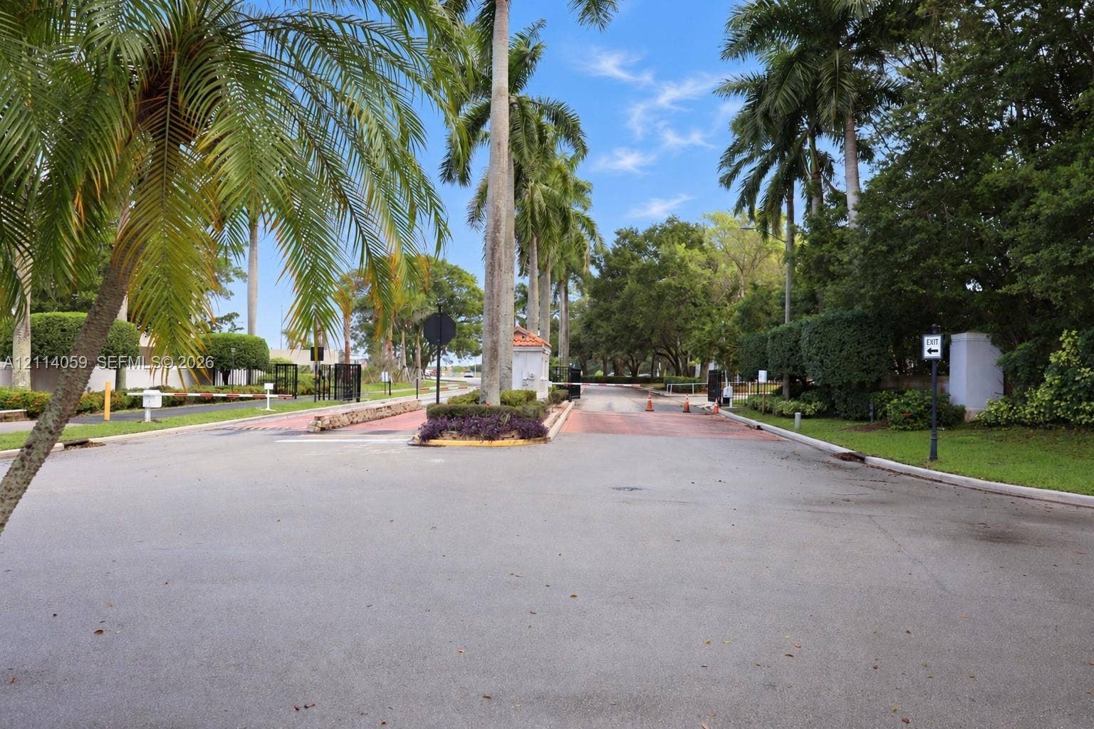 8023 N Tranquility Lake Drive, Delray Beach, FL 33446 Gated entrance featuring a paved roadway, manicured landscaping, and mature palm trees