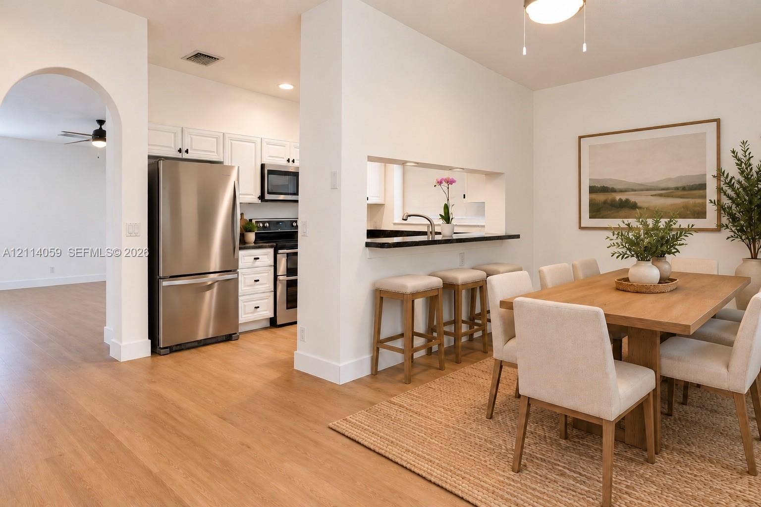 8023 N Tranquility Lake Drive, Delray Beach, FL 33446 Kitchen featuring white cabinetry, stainless steel appliances, and a pass-through bar with a dark countertop, complemented by light wood-finish flooring and an arched entryway