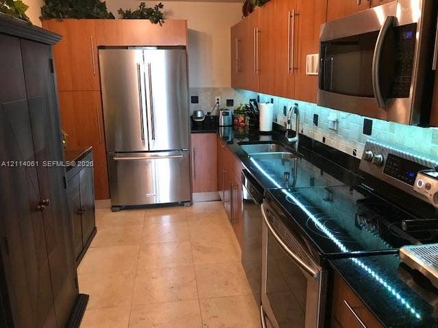 3001 S Ocean Drive, #727, Hollywood, FL 33019 Kitchen featuring natural wood-finish cabinetry, dark solid-surface countertops, light stone tile flooring, under-cabinet lighting, and stainless steel appliances