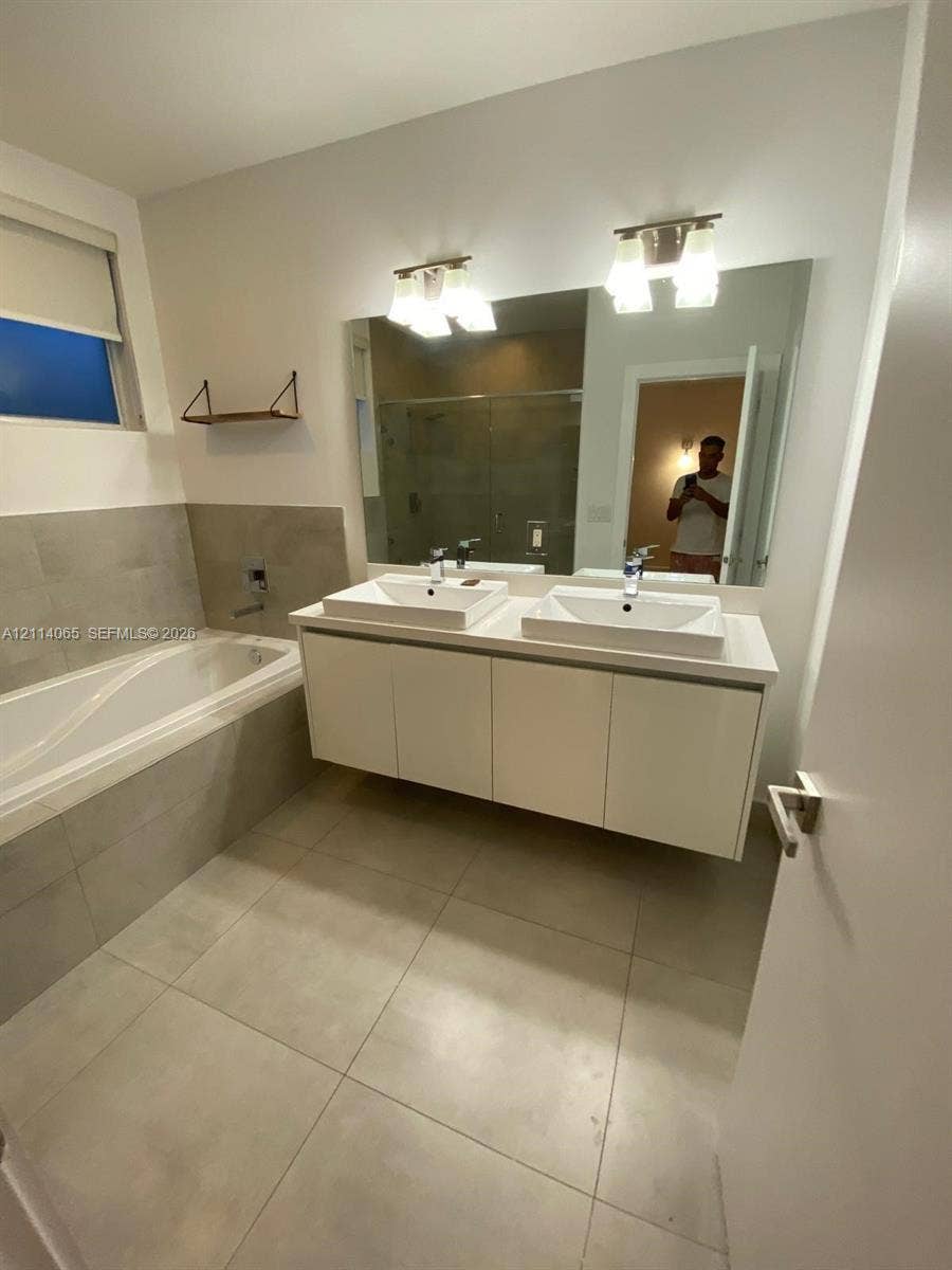 Floating white vanity with double rectangular vessel sinks, quartz countertop, oversized wall-mounted mirror, and tile-surround soaking tub