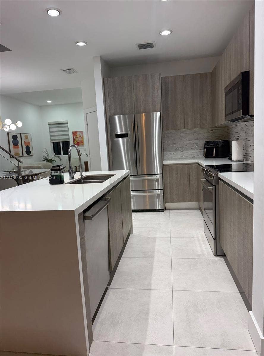 Kitchen featuring flat-panel cabinetry, a quartz waterfall island, large-format tile flooring, stainless steel appliances, and recessed lighting