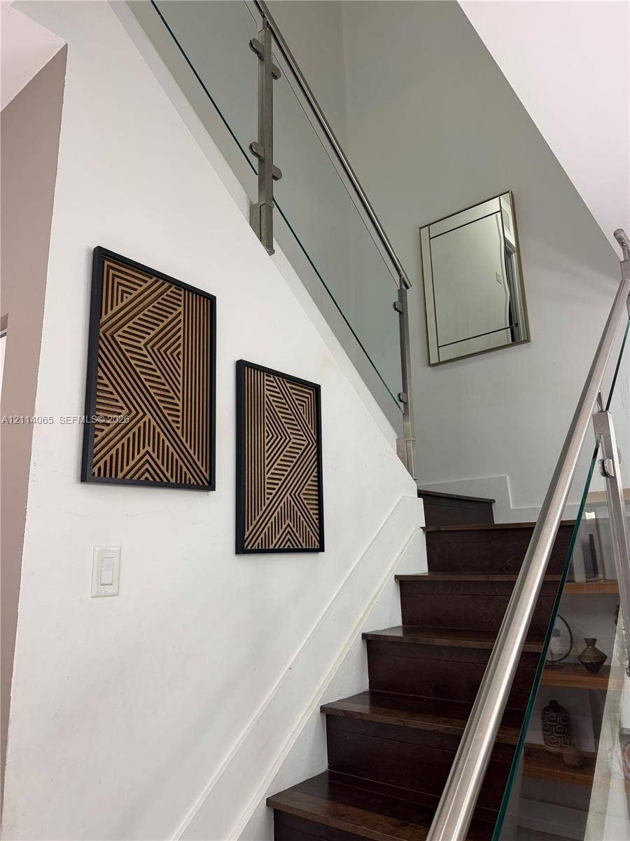 Staircase featuring dark-tone wood treads, a glass railing system, and a metallic handrail