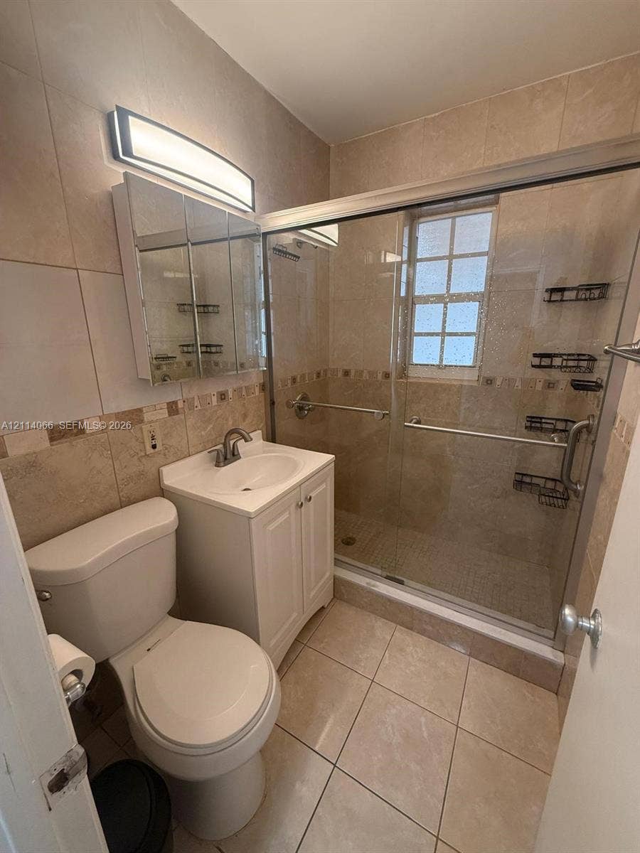 Bathroom featuring a glass-enclosed shower, tiled walls with a decorative accent border, a pedestal-style vanity with white cabinetry, and a mirrored medicine cabinet