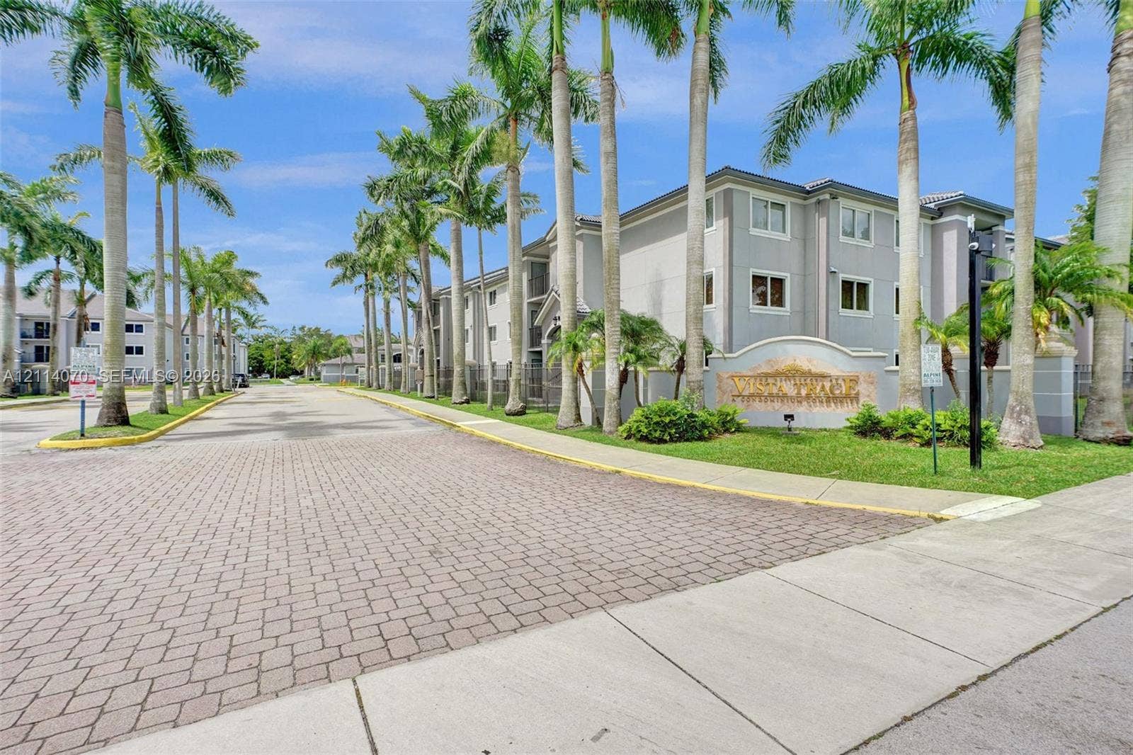 15400 SW 284th Street, #1204, Homestead, Homestead, FL 33033 Multi-story residential buildings featuring light-toned masonry exteriors, paver-style roadway, mature palm trees, and manicured landscaping