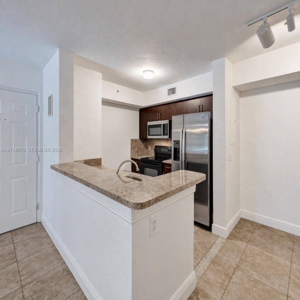 15400 SW 284th Street, #1204, Homestead, Homestead, FL 33033 Kitchen featuring a peninsula with a stone-finish countertop, stainless steel refrigerator, built-in microwave, dark wood-finish cabinetry, and tile flooring
