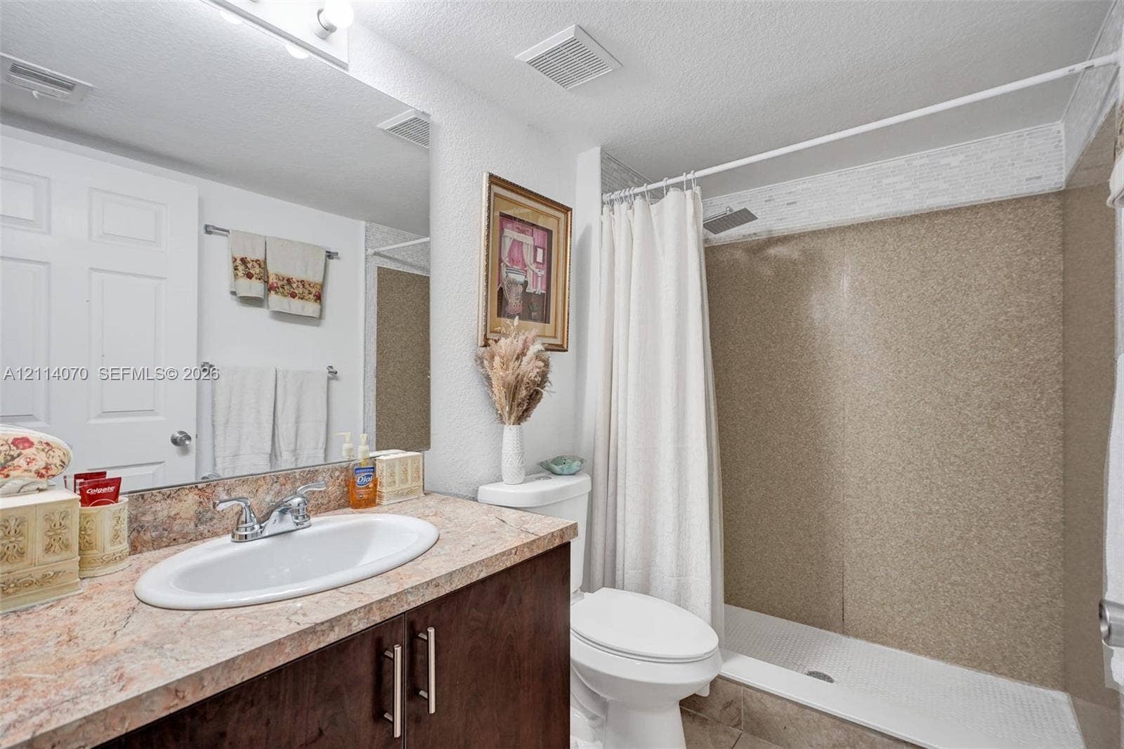 15400 SW 284th Street, #1204, Homestead, Homestead, FL 33033 Bathroom featuring a vanity with a stone-finish countertop, oval drop-in sink, and dark wood-tone cabinetry, complemented by a walk-in shower with textured wall surround and an overhead showerhead