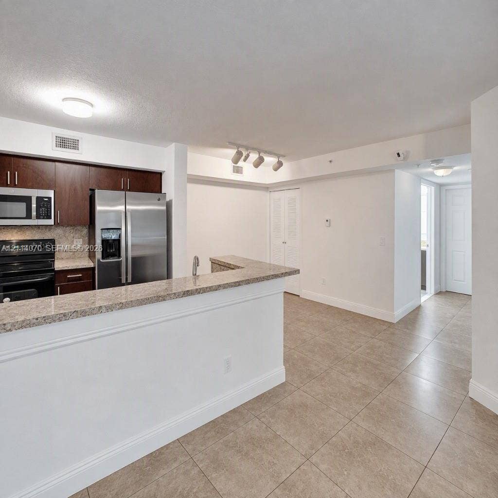 15400 SW 284th Street, #1204, Homestead, Homestead, FL 33033 Kitchen featuring dark wood cabinetry, stone-finish countertops, stainless steel appliances, a peninsula with a sink, and tile flooring