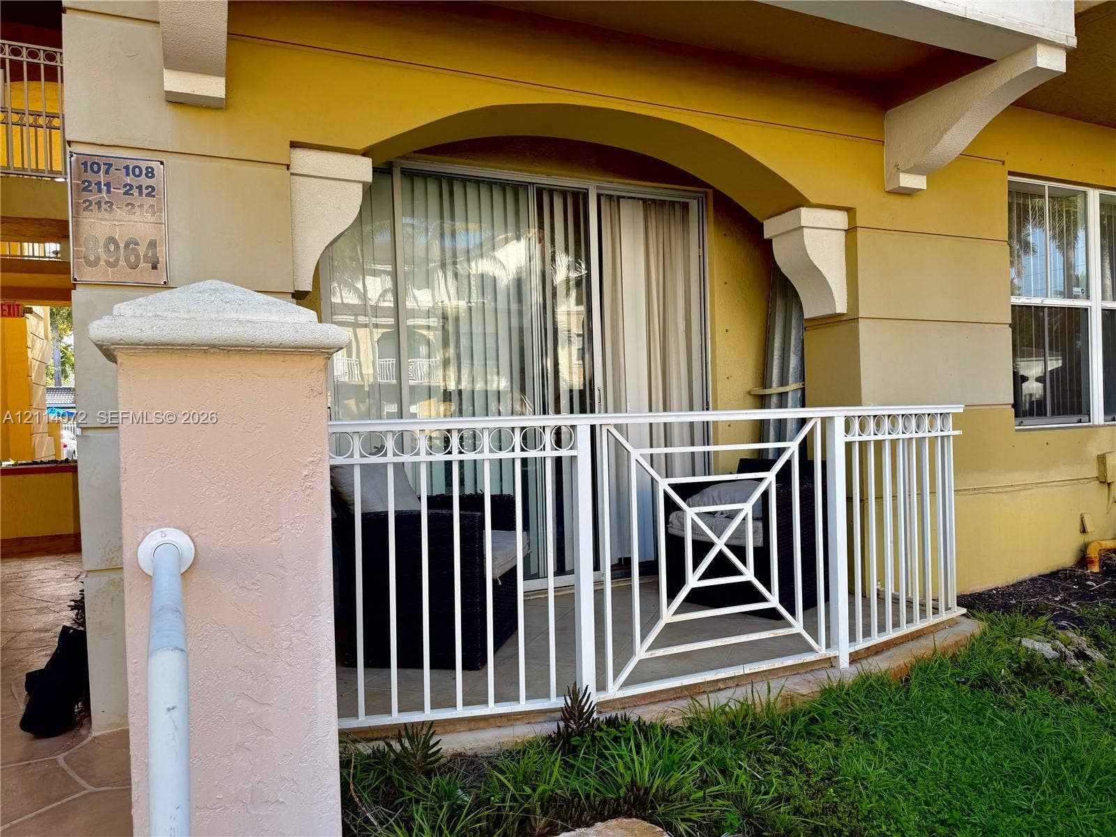 8964 W Flagler Street, #107, Miami, Miami, FL 33174 Covered ground-level patio featuring a white metal railing, arched stucco architectural detailing, and glass sliding doors