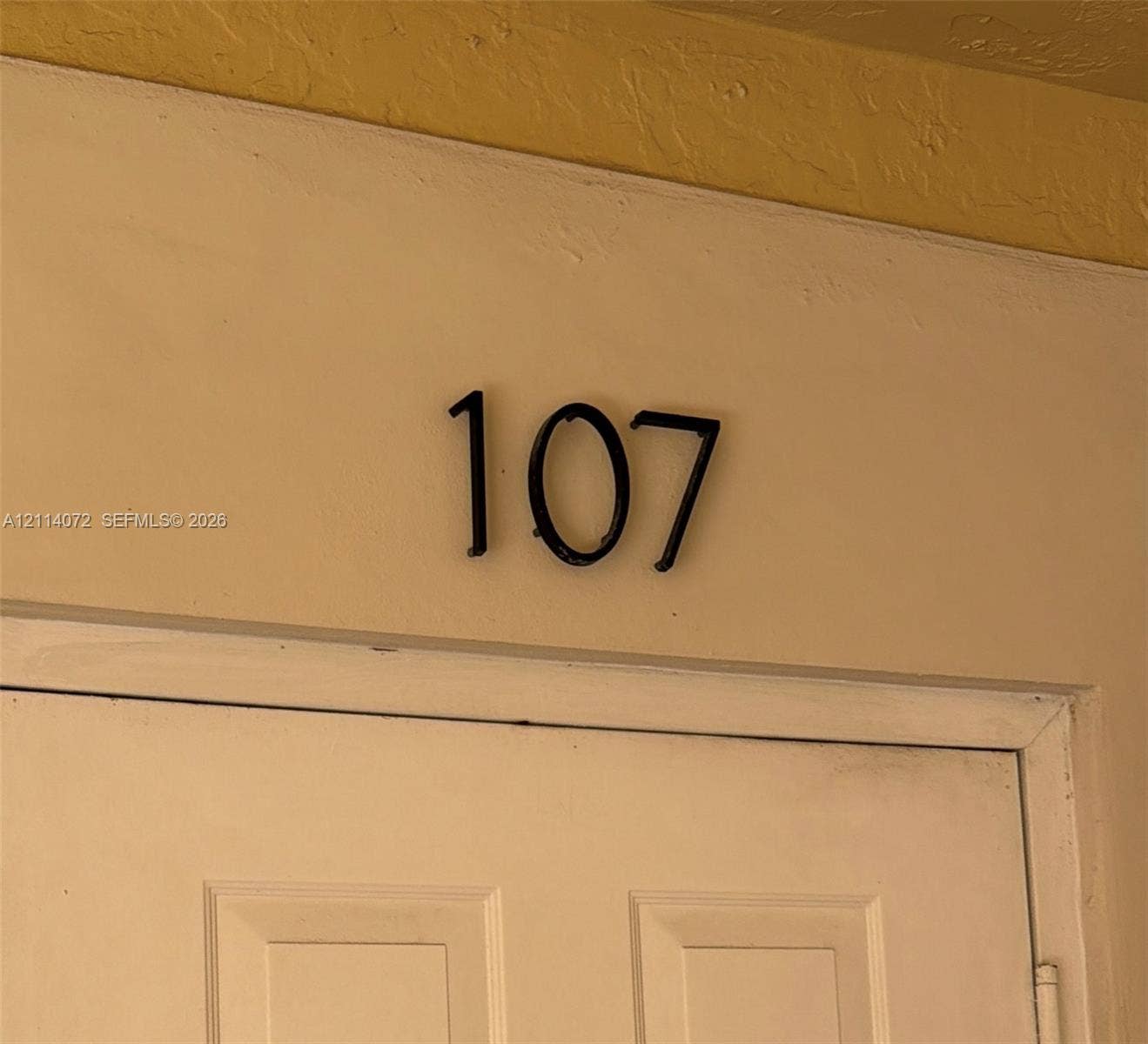 8964 W Flagler Street, #107, Miami, Miami, FL 33174 Matte black numeric address signage mounted on a neutral-toned exterior wall above a paneled door
