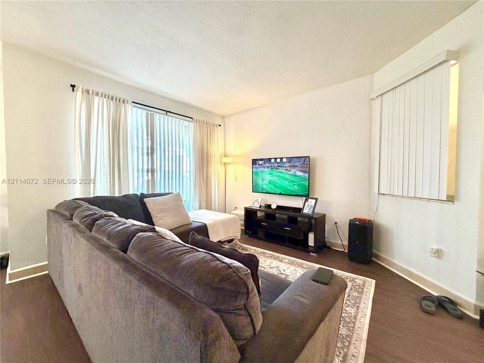 8964 W Flagler Street, #107, Miami, Miami, FL 33174 Neutral-toned living space featuring wood-finish flooring, dual-aspect windows, and vertical blinds