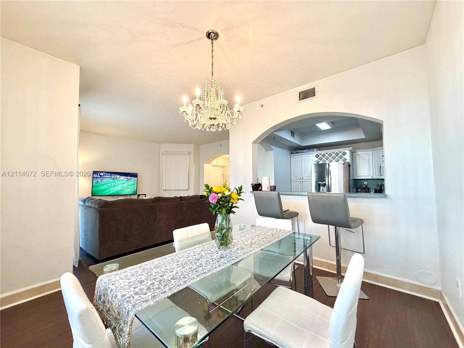 8964 W Flagler Street, #107, Miami, Miami, FL 33174 Dining area featuring wood-finish flooring, an ornate crystal chandelier, and a decorative arched pass-through window with a built-in breakfast bar