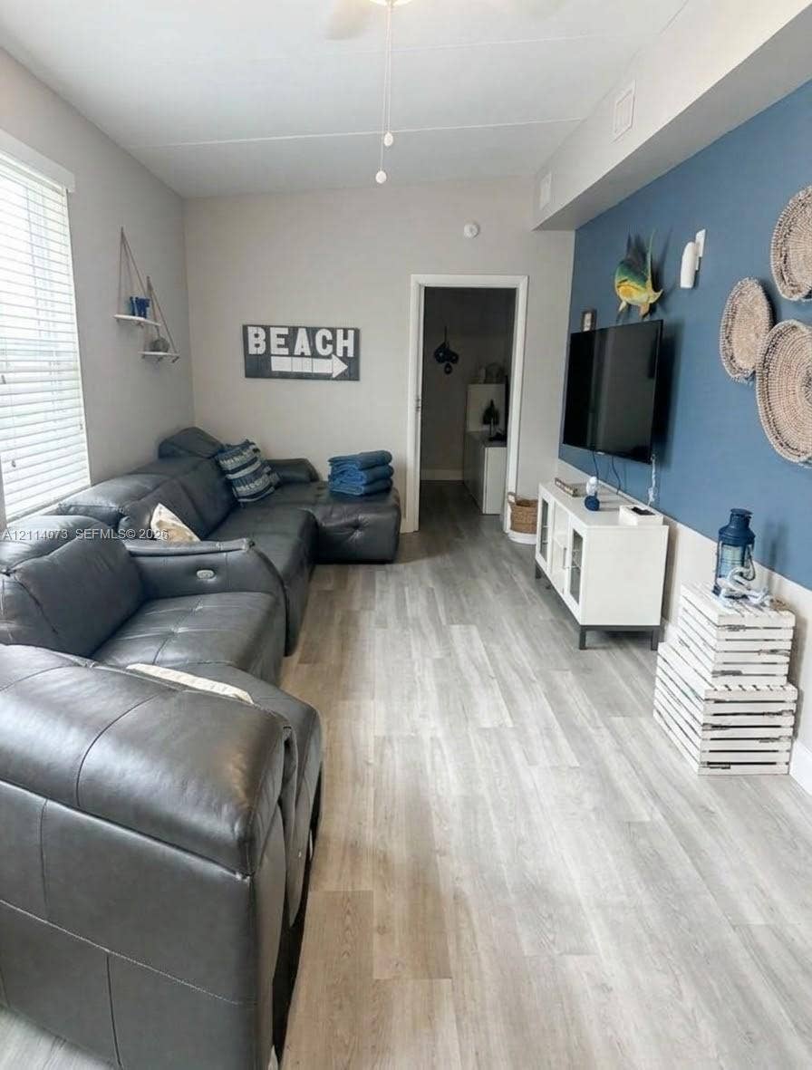 Living area featuring wood-finish flooring, a bold blue accent wall, and horizontal blinds