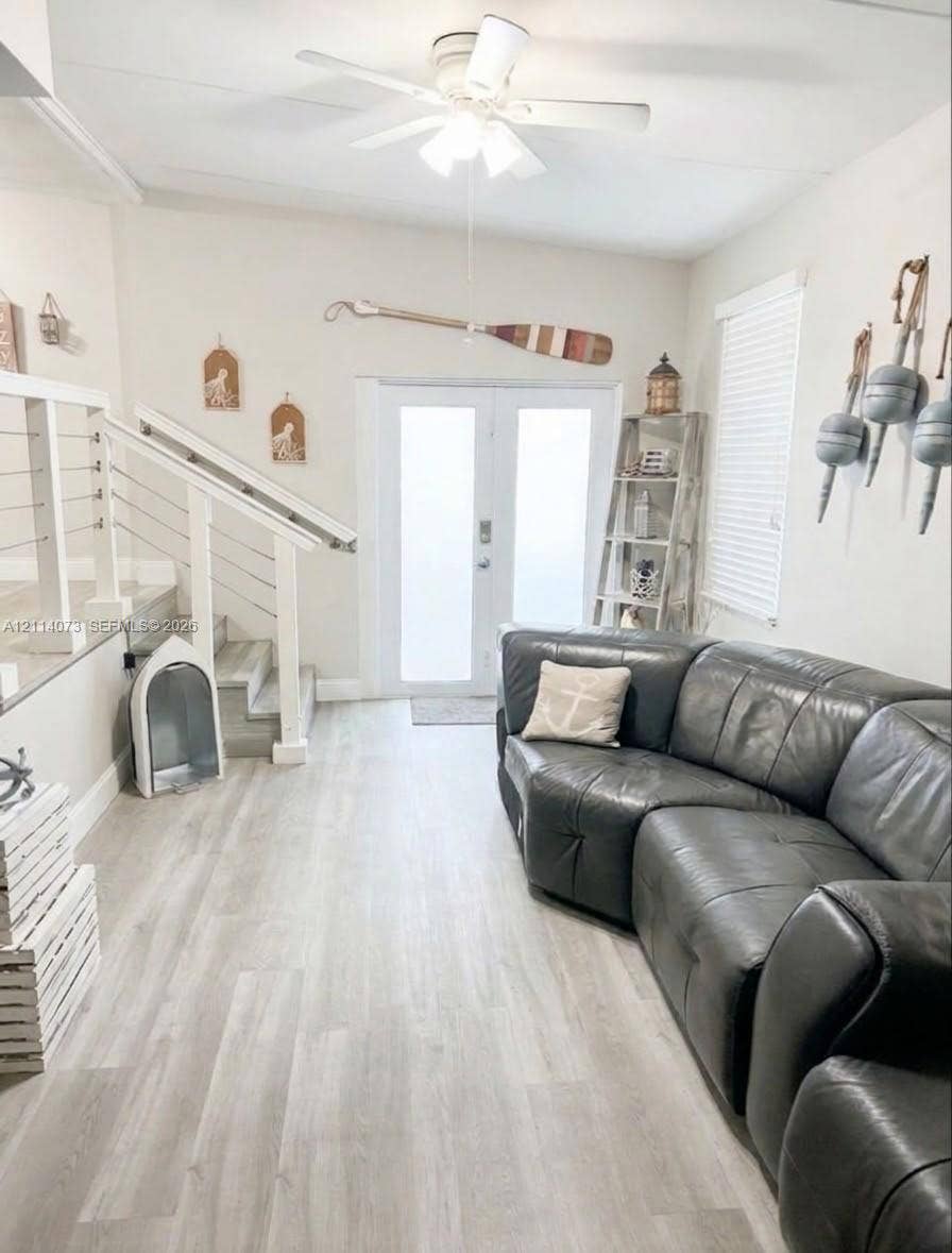 Double entry doors with frosted glass panels, wood-finish flooring, staircase with white railing and cable balusters, and a ceiling-mounted light fixture with fan