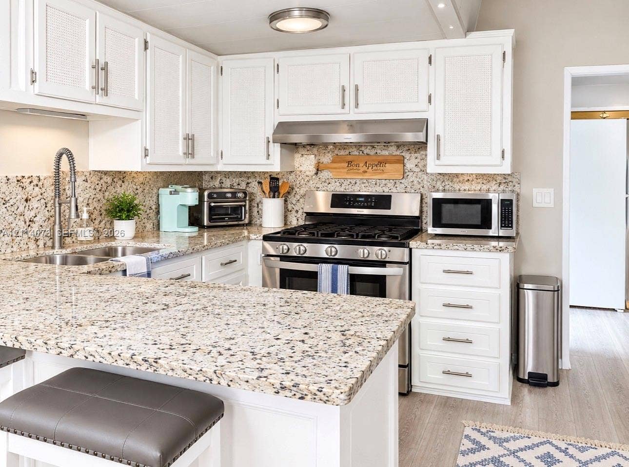 Kitchen featuring white cabinetry with textured door panels, stone-finish countertops, stainless steel appliances including a gas range, and a high-arc pull-down faucet
