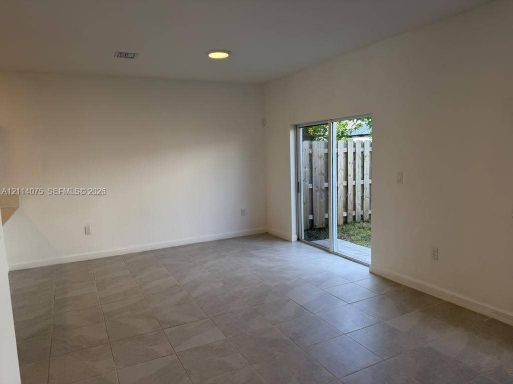 2659 SE 11th Street, Homestead, FL 33035 Interior space featuring large-format neutral floor tile, recessed ceiling lighting, and sliding glass doors opening to a fenced outdoor area