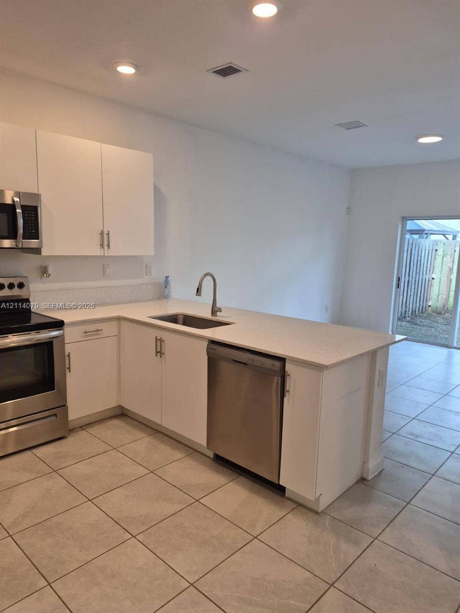 2659 SE 11th Street, Homestead, FL 33035 Kitchen featuring white cabinetry, light-toned stone-finish countertops, stainless steel appliances, recessed ceiling lighting, and tile flooring