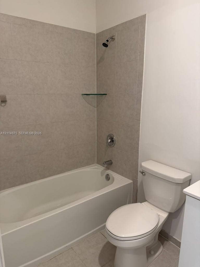 2659 SE 11th Street, Homestead, FL 33035 Full-size bathtub with integrated shower, neutral-toned wall tile surround, built-in glass corner shelving, chrome-finish plumbing fixtures, and standard-height porcelain commode