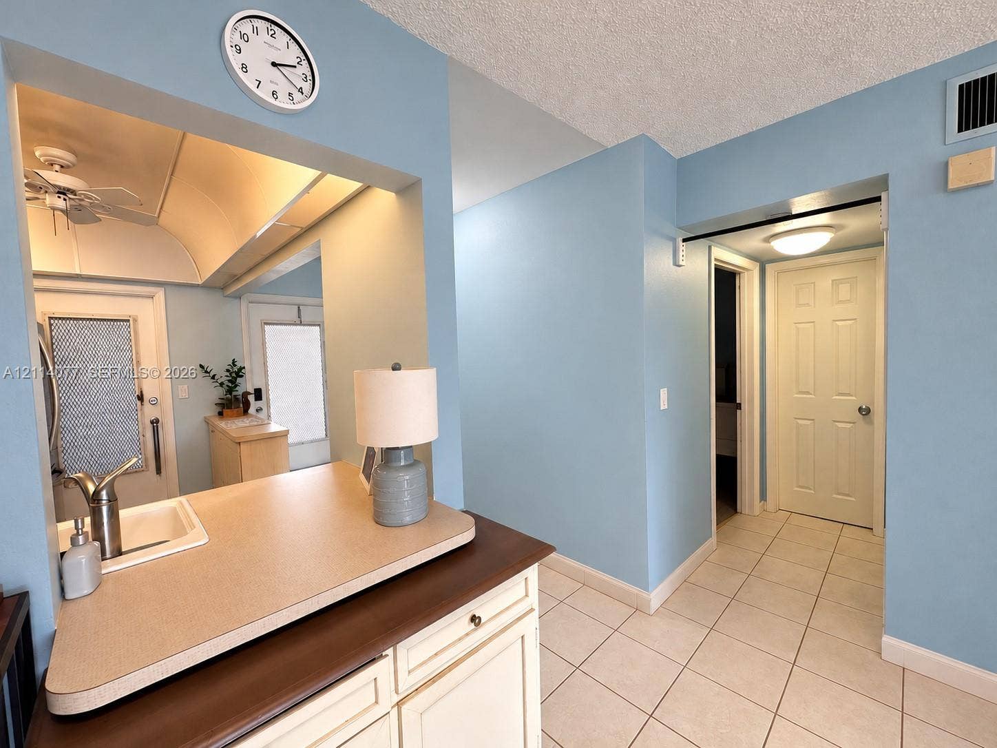 465 Paradise Isle Boulevard, #206, Hallandale Beach, Hallandale Beach, FL 33009 Kitchen passthrough featuring a solid-surface countertop and integrated sink with a chrome gooseneck faucet, accompanied by light-toned cabinetry and ceramic tile flooring