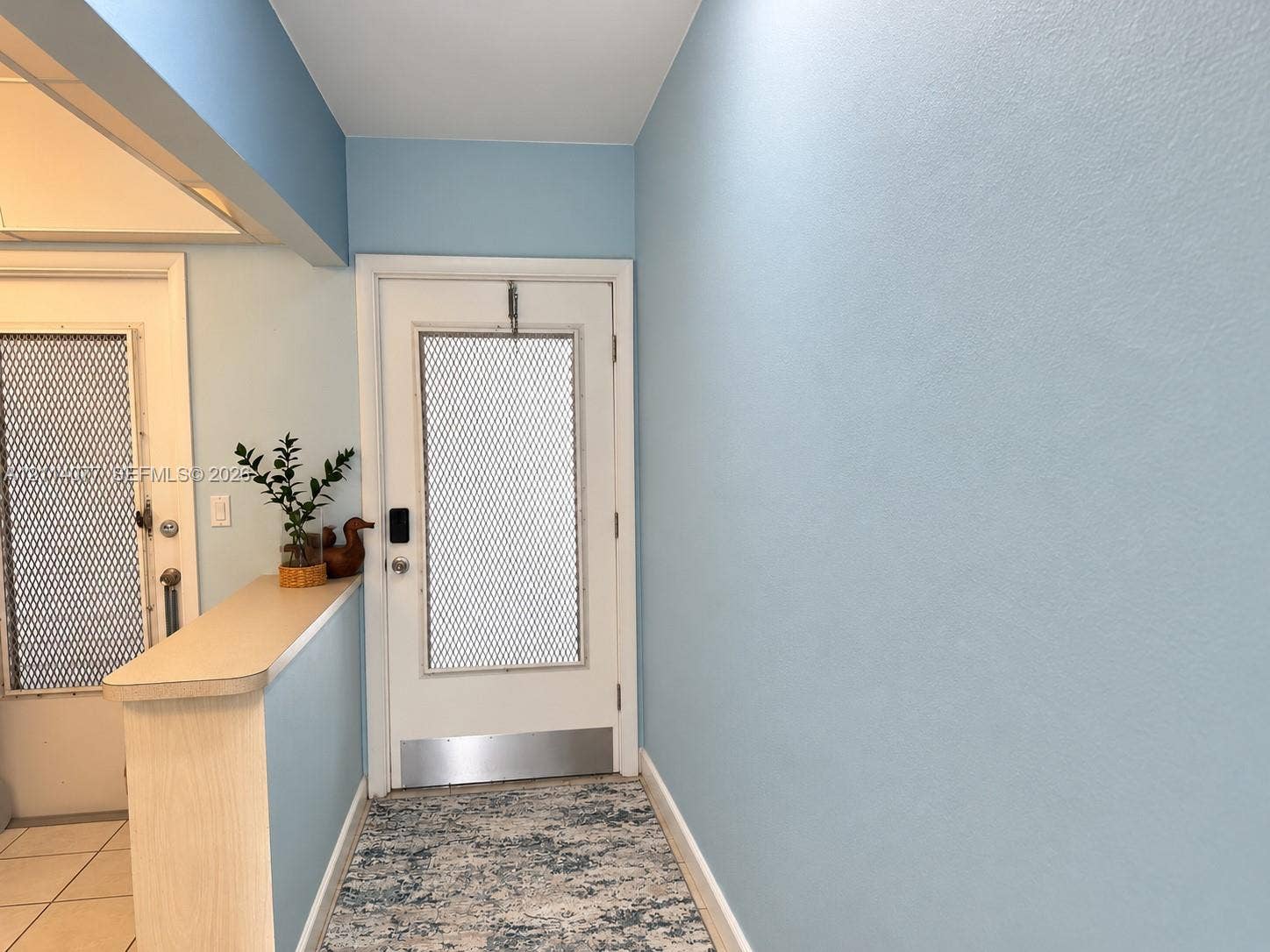 465 Paradise Isle Boulevard, #206, Hallandale Beach, Hallandale Beach, FL 33009 Entrance featuring a white door with a metal kickplate, decorative mesh insert, and integrated keypad lock, complemented by a solid-surface half-wall divider and overhead skylight