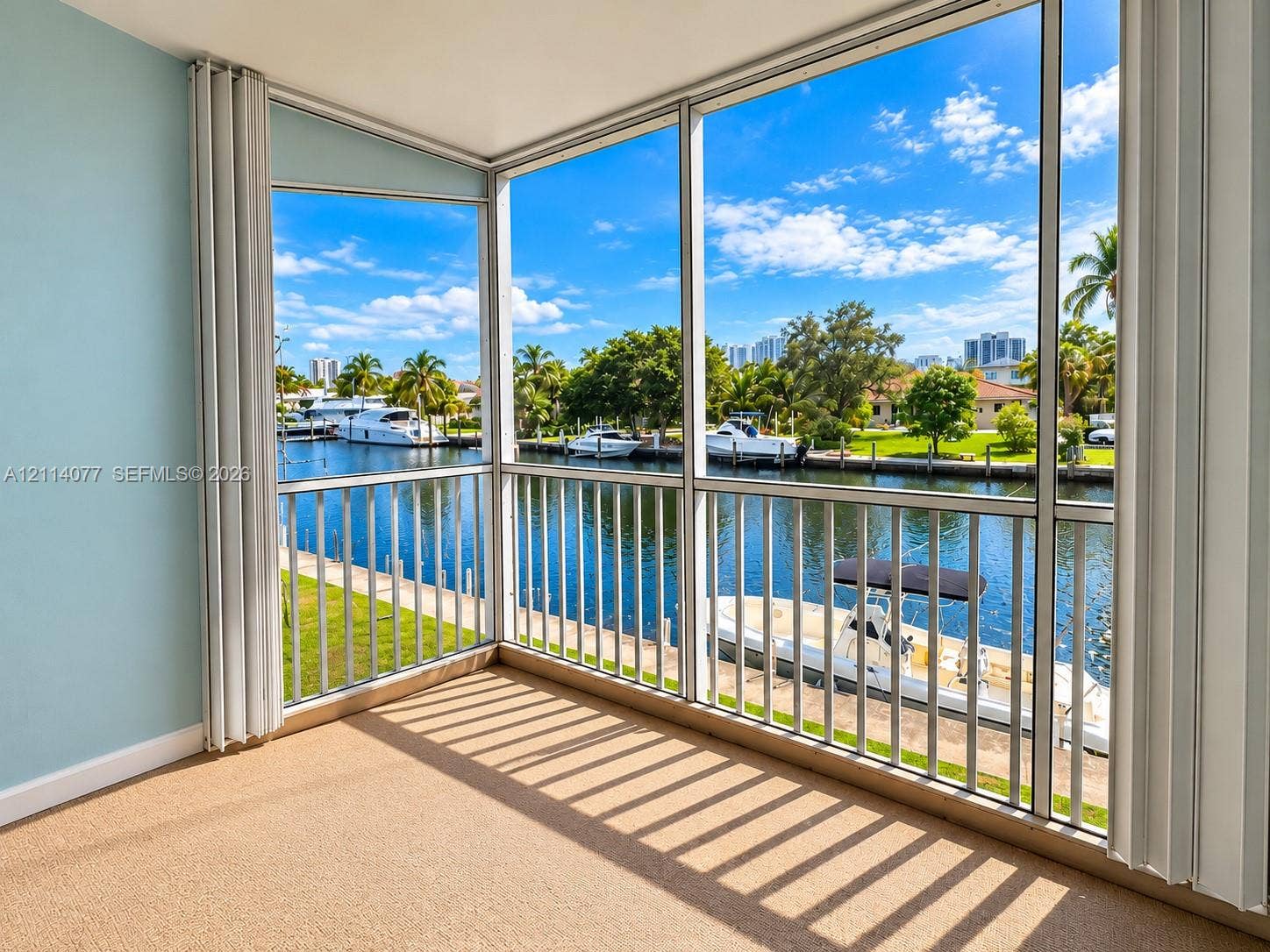465 Paradise Isle Boulevard, #206, Hallandale Beach, Hallandale Beach, FL 33009 Enclosed balcony featuring floor-to-ceiling screened windows, white metal framing, and a bulkhead ceiling, overlooking a canal with maritime activity