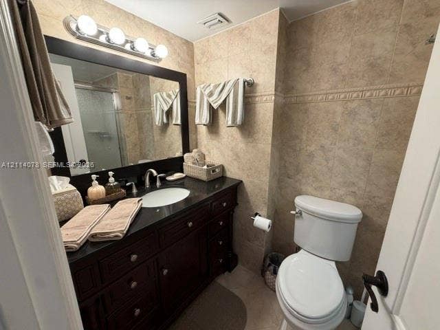Dark-finish wooden cabinetry with integrated storage, dark stone-surfaced countertop, undermount sink, multi-bulb vanity lighting, and full-height wall tiling
