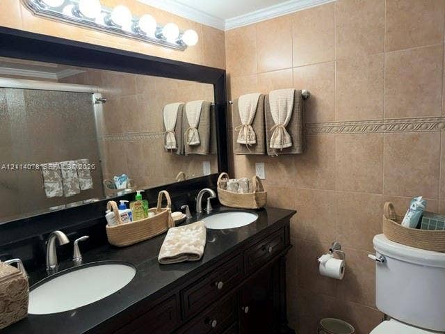 Double vanity featuring dark wood-finish cabinetry, a solid-surface countertop with dual under-mount sinks, polished chrome hardware, and full-width wall mirror with a decorative border