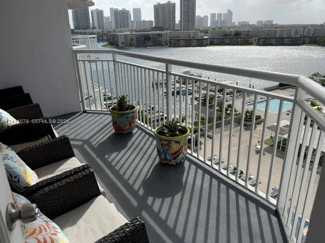 Covered balcony with white metal railings, grey surface flooring, and expansive water and urban skyline backdrop