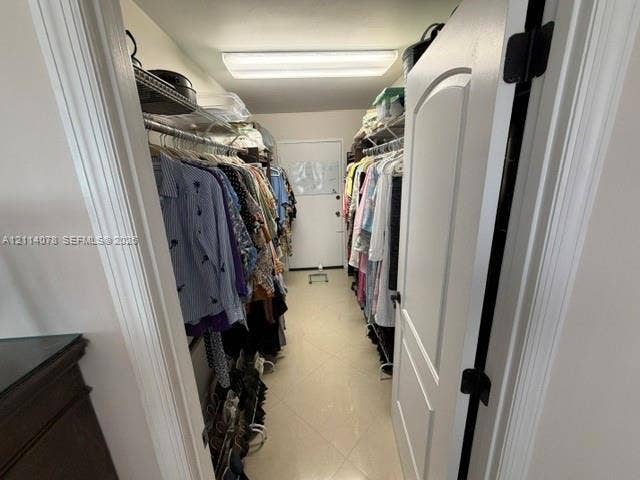 Walk-in closet featuring dual tiers of wire shelving, ceramic tile flooring, a solid-core interior door, and overhead flush-mount lighting