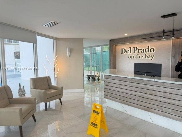Lobby featuring polished tile flooring, floor-to-ceiling windows, and a reception desk with wood-slat detailing, stone countertop, and integrated backlighting