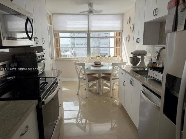 Kitchen featuring white cabinetry, stone-finish countertops, stainless steel appliances, tile flooring, and large windows with integrated blinds