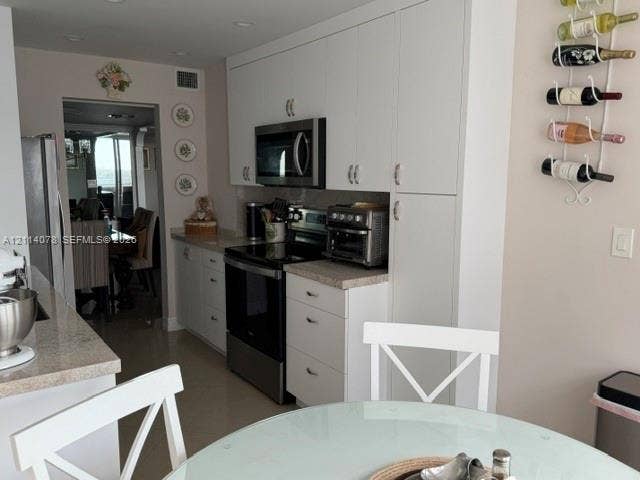 White cabinetry with integrated hardware, stainless steel appliances, neutral stone-finish countertops, and recessed lighting