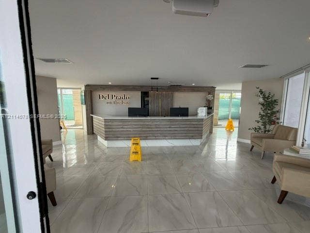 Reception area featuring large-format polished tile flooring, wood-paneled concierge desk with integrated lighting, and high-contrast signage