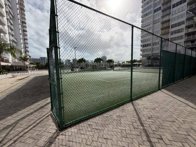 Tennis court featuring a green surface, chain-link perimeter fencing, and concrete paver decking