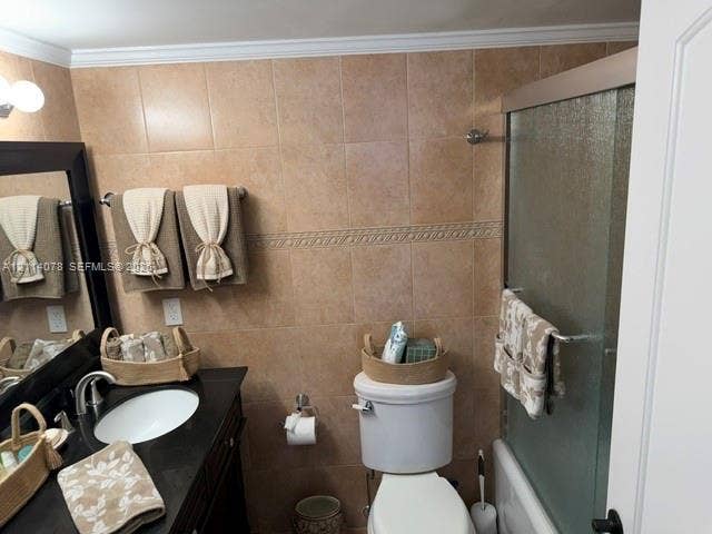 Bathroom featuring a dark wood-finish vanity with a contrasting solid surface countertop, an undermount sink, ceramic wall tiling with decorative accent trim, and a framed shower enclosure