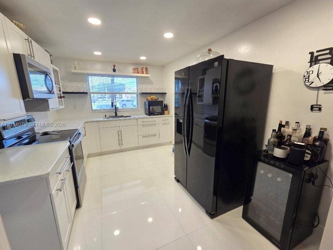 9241 Sunrise Lakes Boulevard, #109, Sunrise, FL 33322 Kitchen featuring white cabinetry, solid-surface countertops, recessed ceiling lighting, light-toned tile flooring, and integrated black kitchen appliances