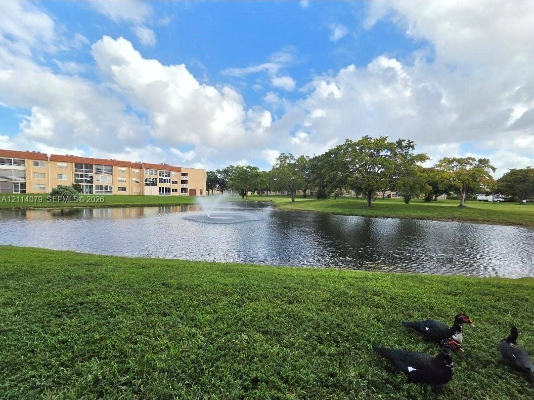 9241 Sunrise Lakes Boulevard, #109, Sunrise, FL 33322 Waterfront pond with a built-in fountain, surrounding green space, and mature trees