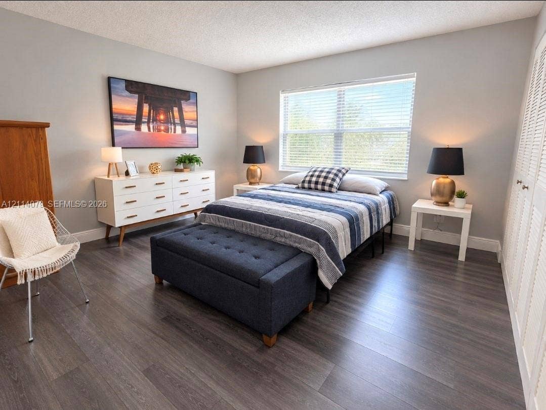 9241 Sunrise Lakes Boulevard, #109, Sunrise, FL 33322 Bedroom featuring wood-finish flooring, a large window with horizontal blinds, and louvered double closet doors