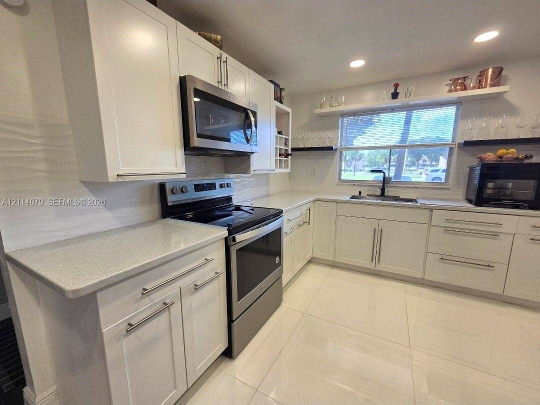 9241 Sunrise Lakes Boulevard, #109, Sunrise, FL 33322 Kitchen featuring white cabinetry, solid-surface countertops, stainless steel appliances, a matte black faucet, and large-format tile flooring