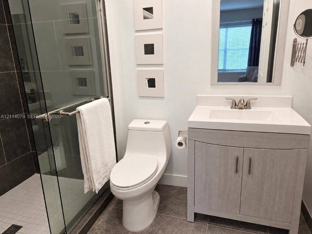 9241 Sunrise Lakes Boulevard, #109, Sunrise, FL 33322 Bathroom featuring a wood-finish vanity with a rectangular sink, glass-enclosed shower with dark tile surround, and neutral floor tile